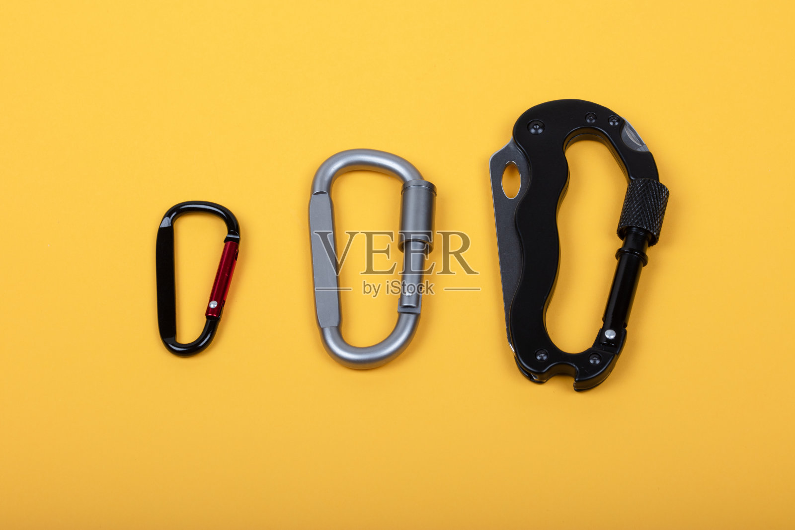 不同类型的金属登山扣排列在黄色背景上 - 冒险装备和安全工具照片摄影图片