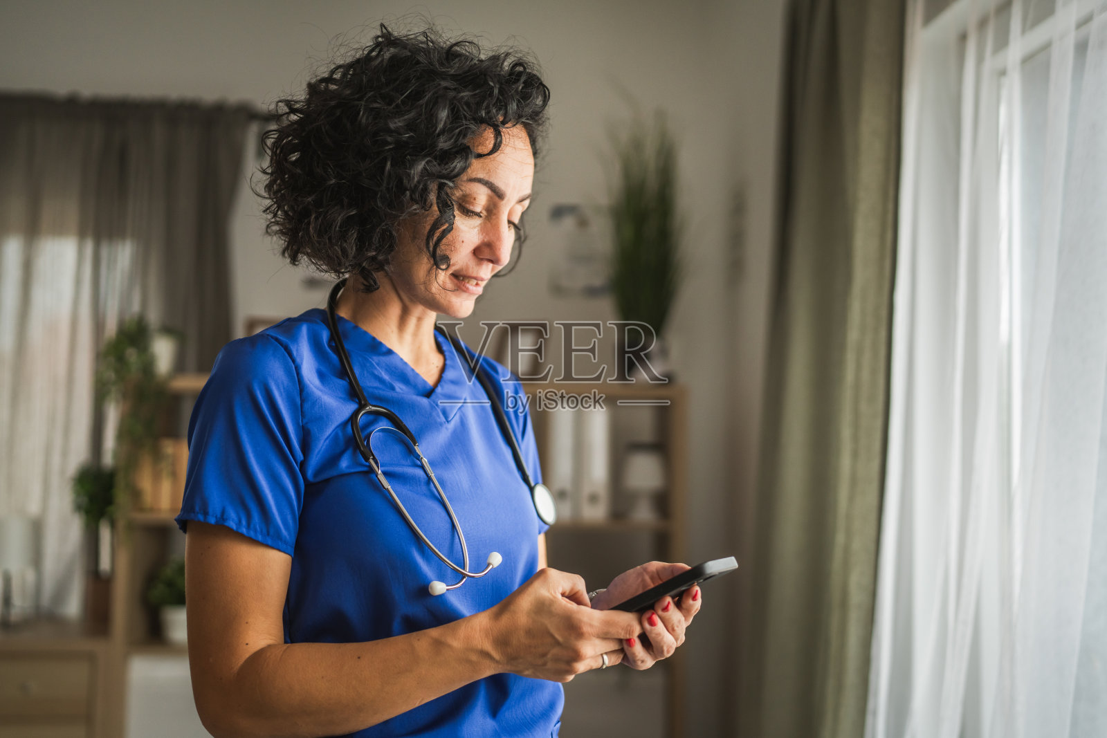 成熟的女性医生在家中站着使用手机照片摄影图片