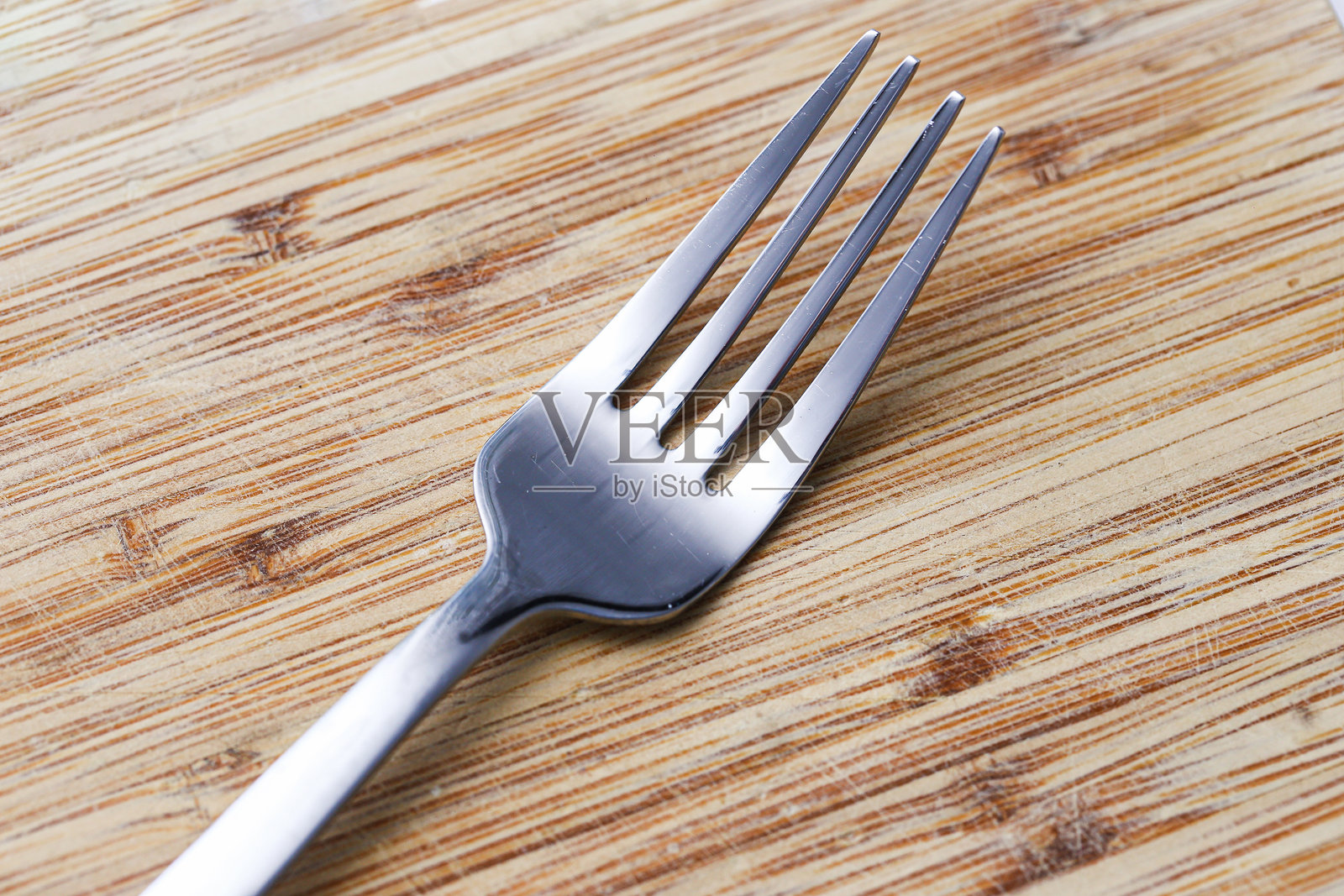 银色叉子放在质朴的木质砧板上。单一餐具孤立在有纹理的木头上。餐具背景。光滑金属与天然木材之间的对比。照片摄影图片