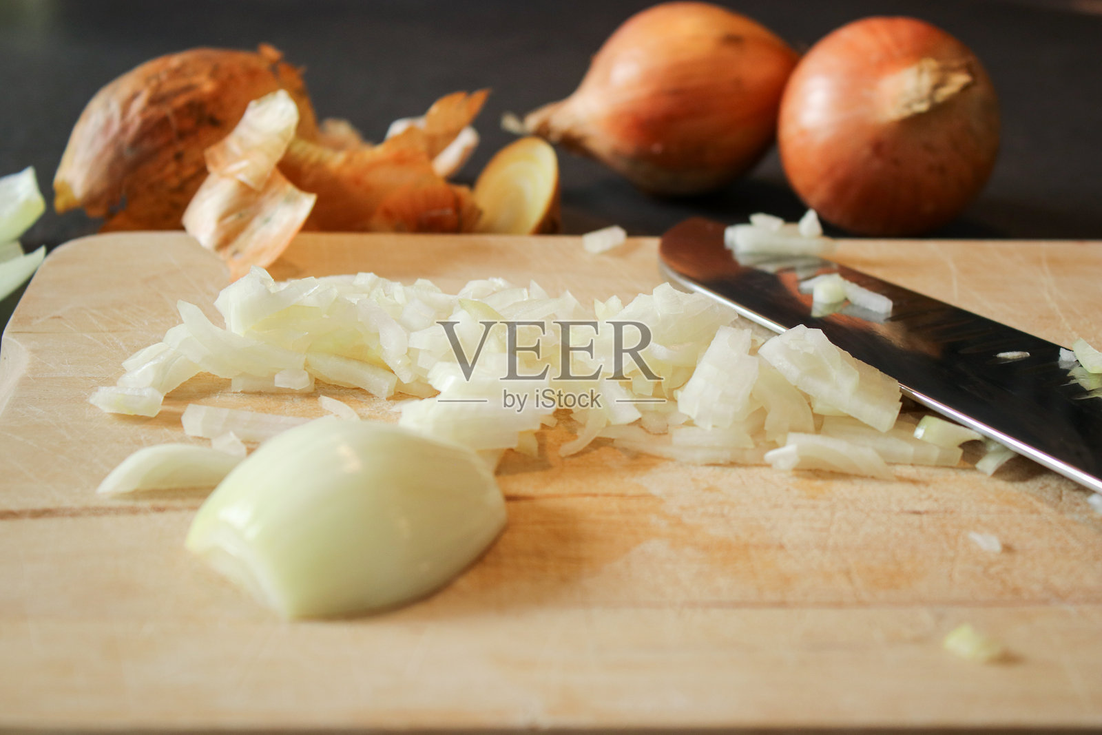 切好的白洋葱特写,放在木砧板上,旁边有一把刀,背景是深灰色的厨房桌子。照片摄影图片