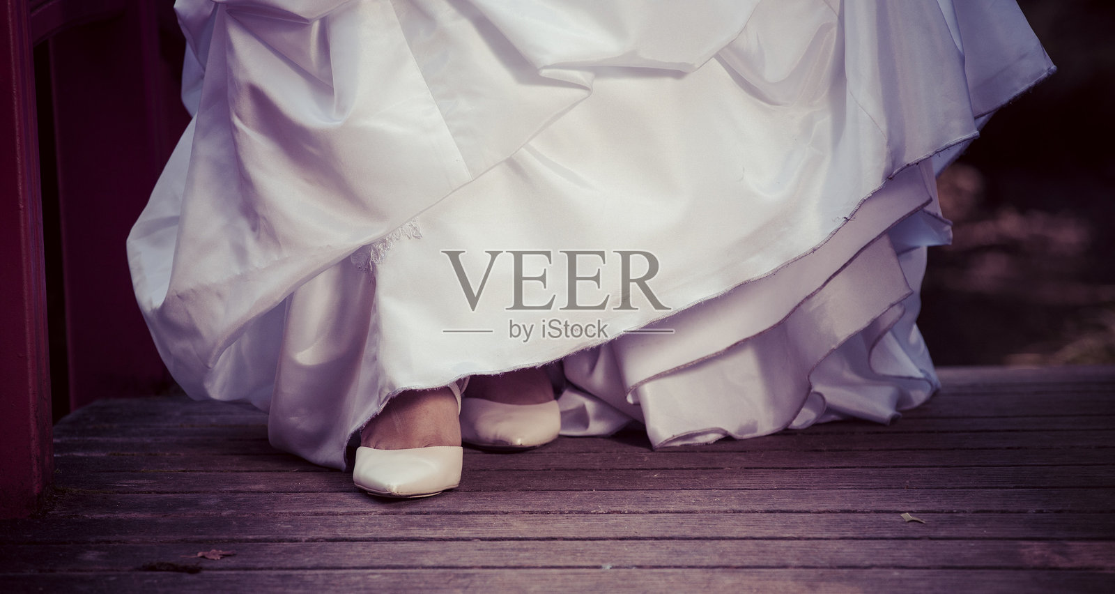 一位新娘身穿精致的婚纱,优雅地走上户外仪式的木质甲板。照片摄影图片