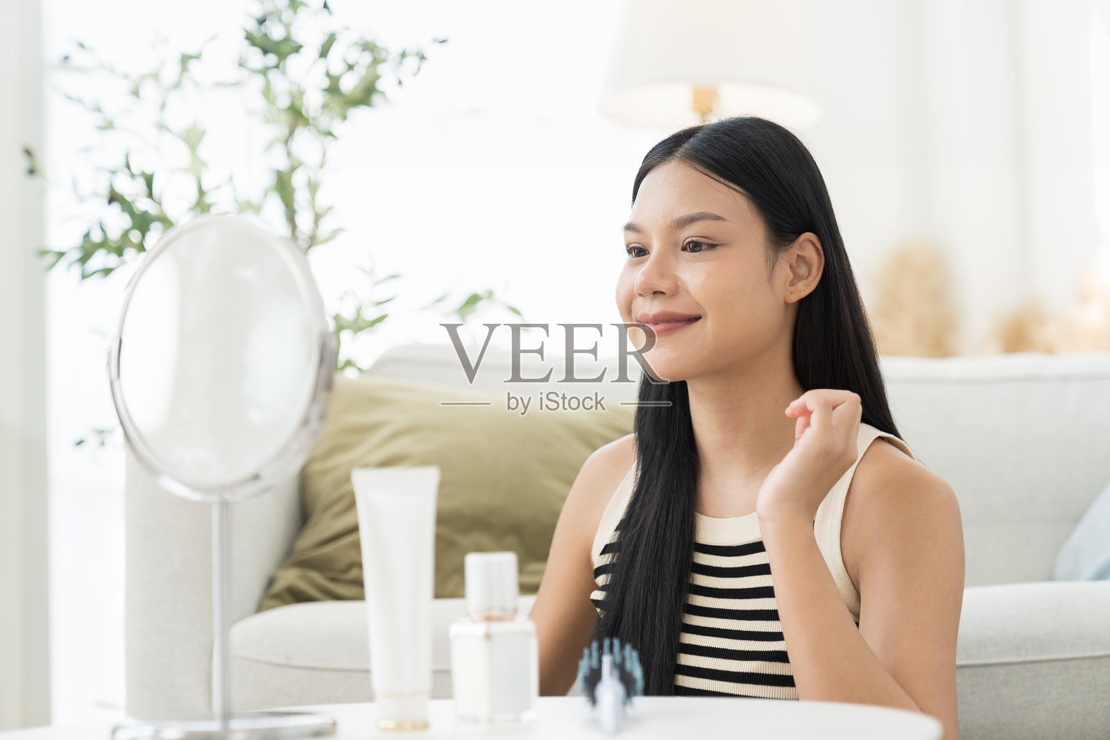 快乐的年轻亚洲美女坐在镜子旁,微笑着看着镜子,用梳子梳理她美丽的头发。照片摄影图片