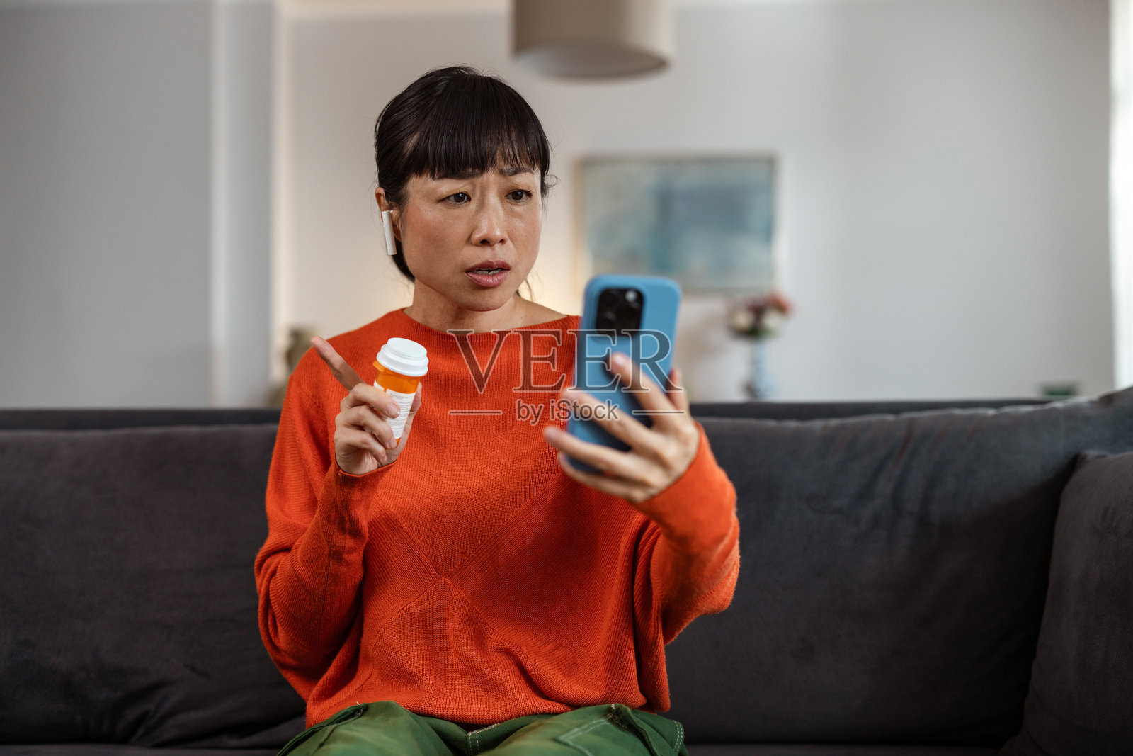 日本女性一边使用耳塞式耳机和智能手机,一边拿着药瓶与医生交谈。照片摄影图片