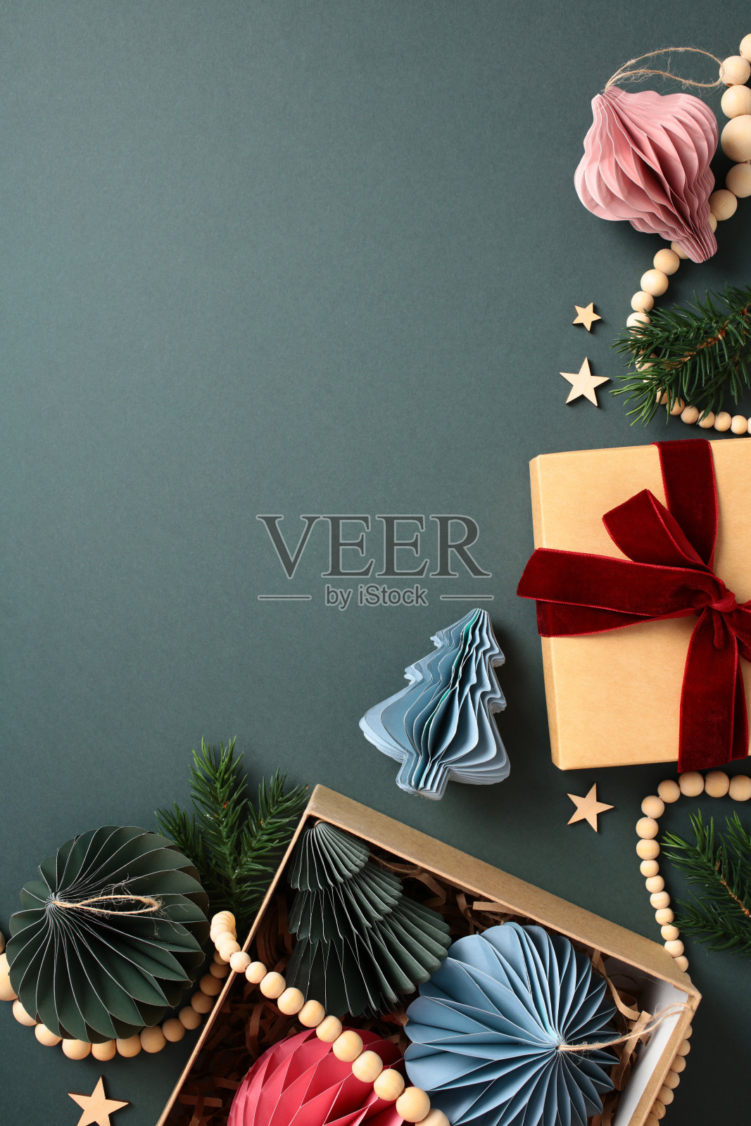 圣诞节平铺的斯堪的纳维亚纸质蜂窝装饰品、冷杉树枝、木珠花环、礼品盒,背景为深绿色。圣诞手工艺,DIY,环保。照片摄影图片