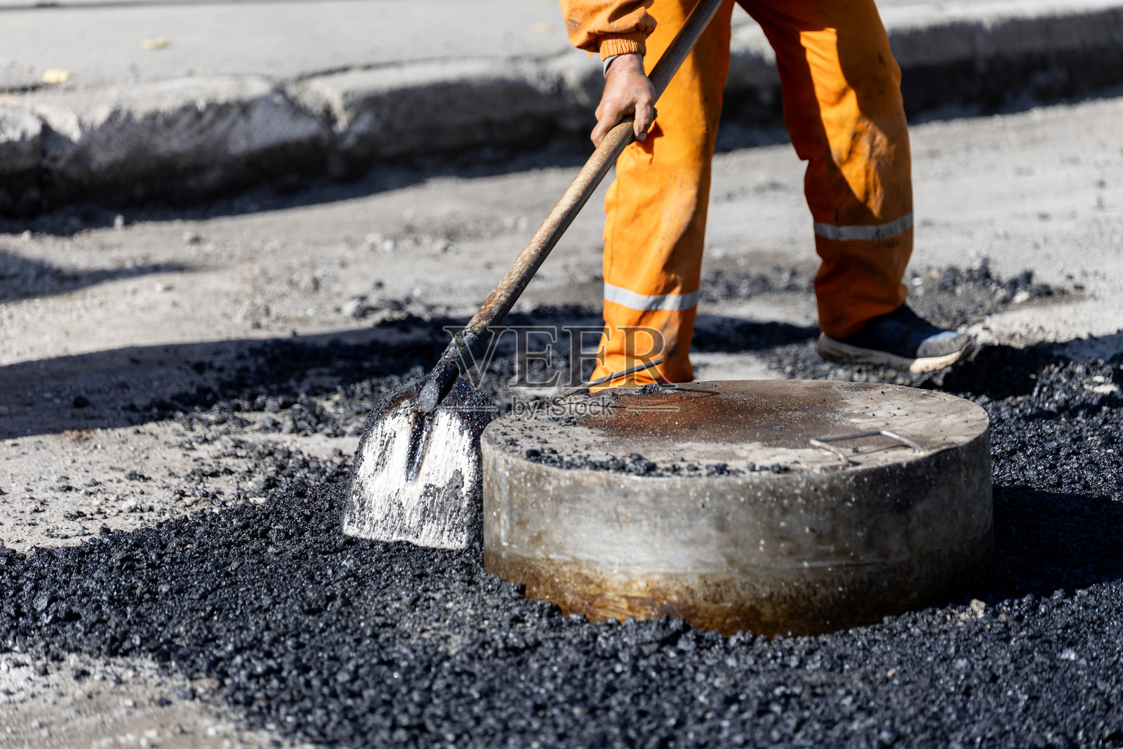 工人在白天的城市街道上修补井盖周围的沥青照片摄影图片