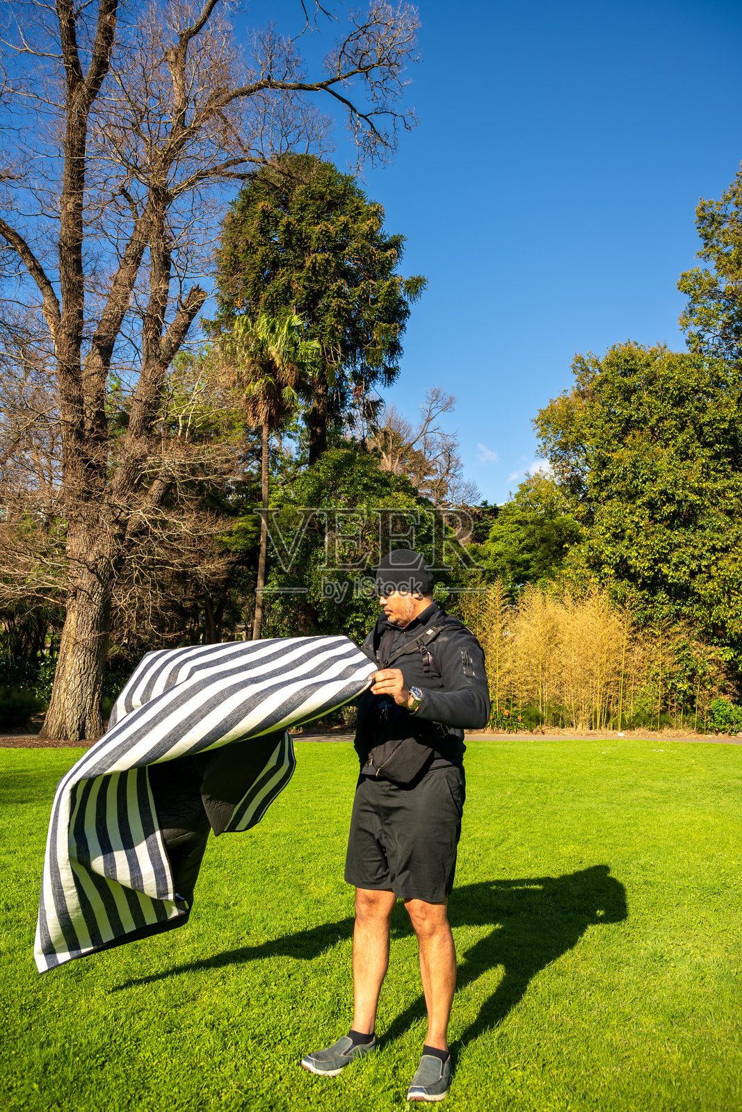 一名男子在澳大利亚维多利亚州墨尔本的菲茨罗伊花园收拾野餐毯,结束了一天的户外活动。照片摄影图片