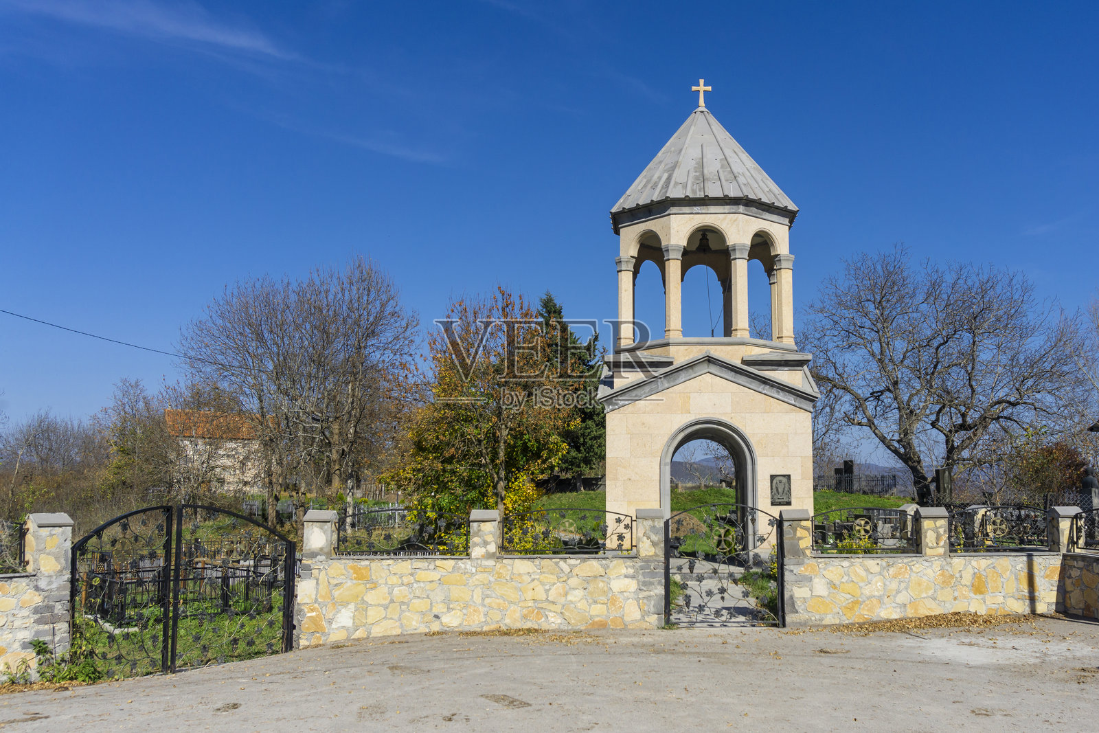 阿布拉梅提村教堂的钟楼。带有葡萄藤图案的铁门,石制围栏。秋天的色彩,蓝天。照片摄影图片
