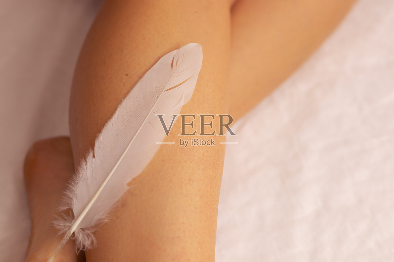 一个人在宁静的室内环境中轻轻地用柔软的羽毛触碰自己的腿。照片摄影图片