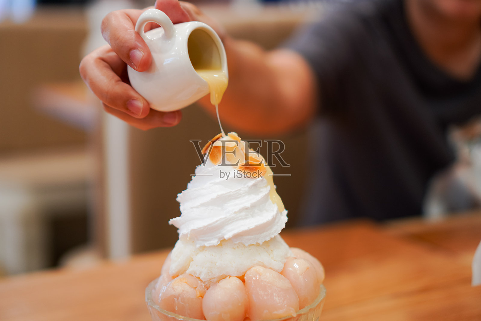 人们在餐桌上把甜炼乳倒在韩式刨冰上,上面撒上荔枝和白色炼乳奶油。照片摄影图片