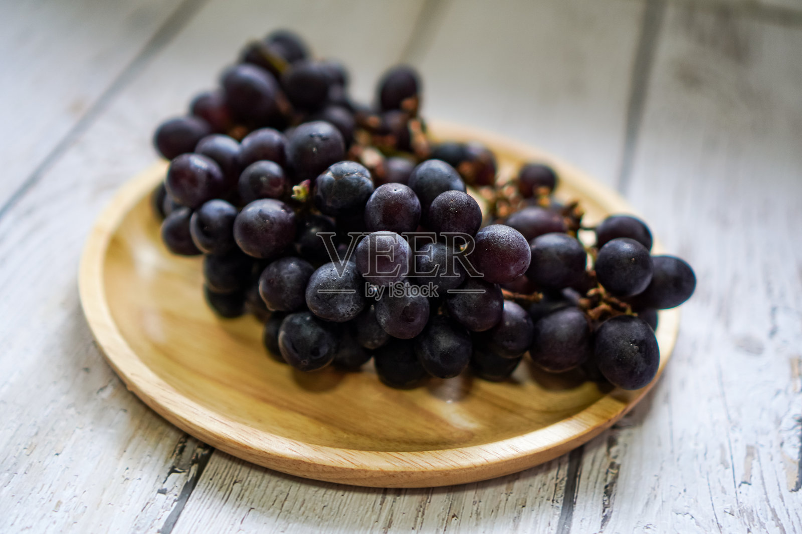 木盘上一串串的黑葡萄。照片摄影图片