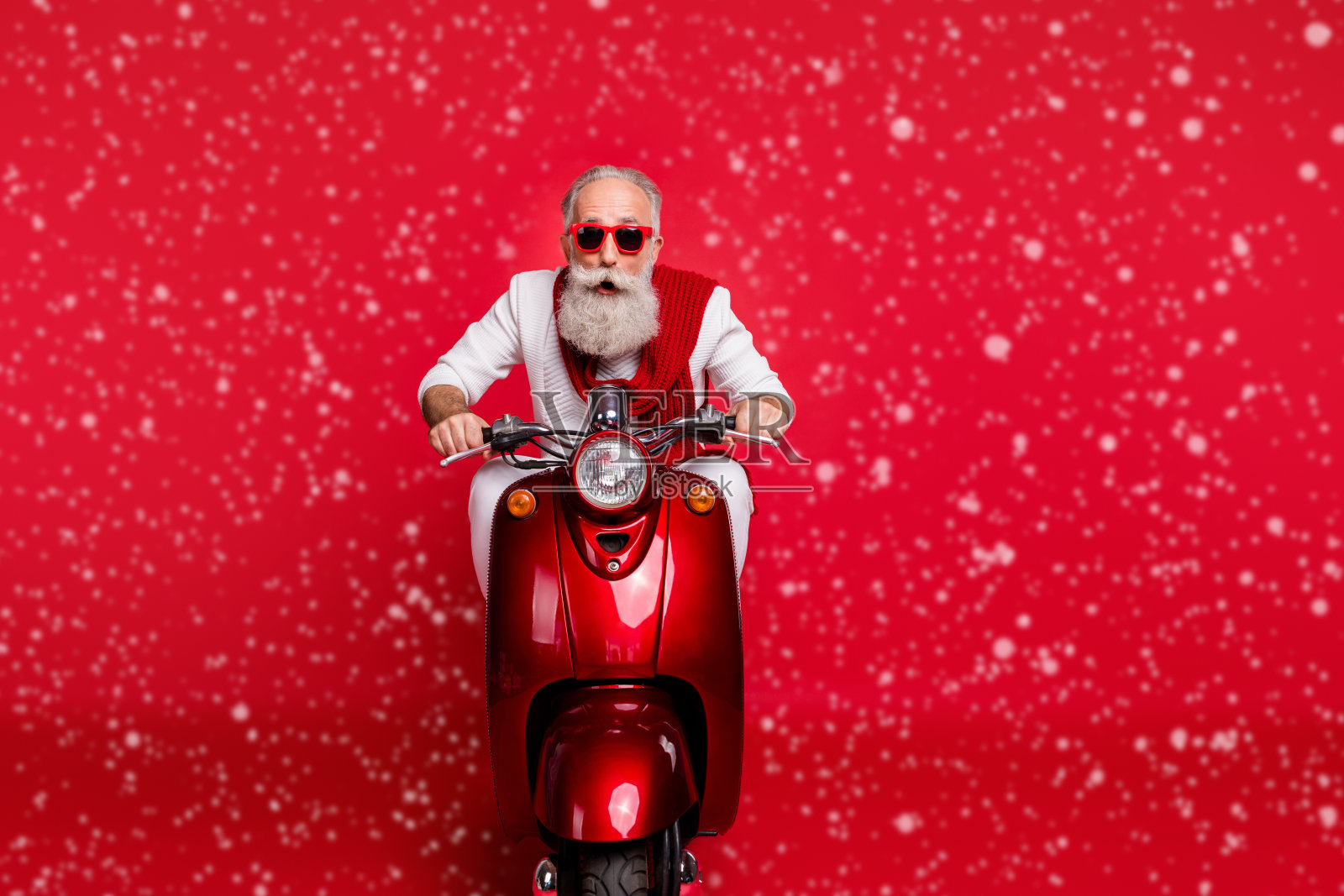 惊讶的老年人佩戴眼镜,骑着自行车,穿着白色毛衣,背景为红色,惊呼“哇,天哪!”照片摄影图片