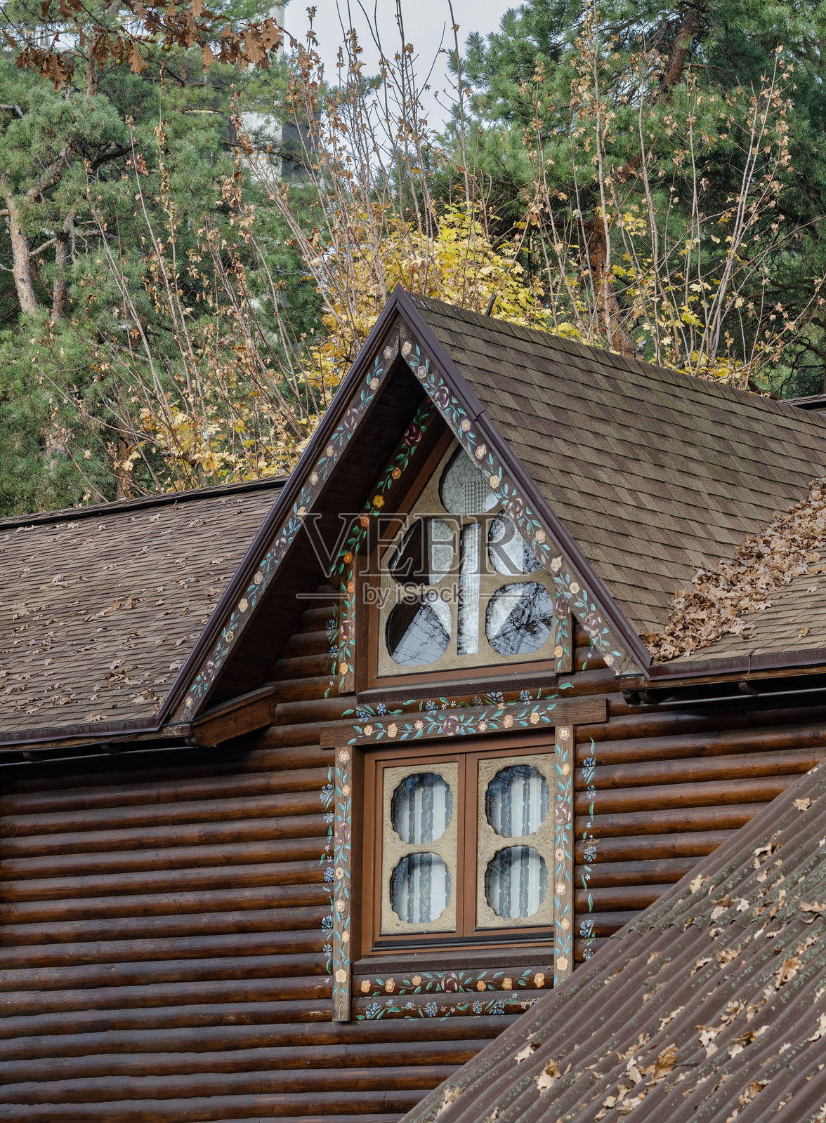 装饰性窗户和屋顶覆盖秋叶的彩绘木屋,背景是一片森林。照片摄影图片