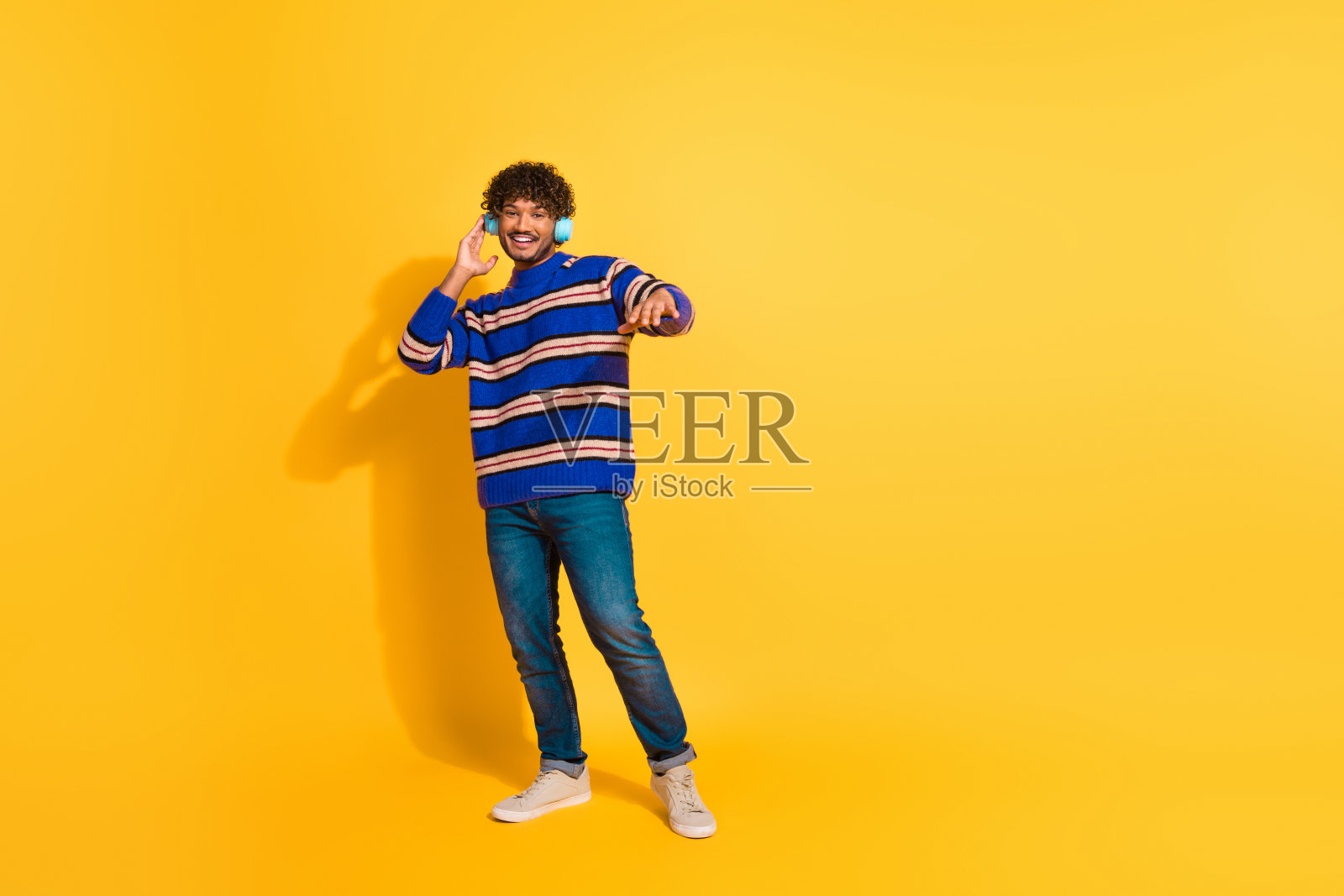 全身照,帅气的年轻男性,佩戴耳机,穿着时尚的蓝色条纹服装,在黄色背景下跳舞。照片摄影图片