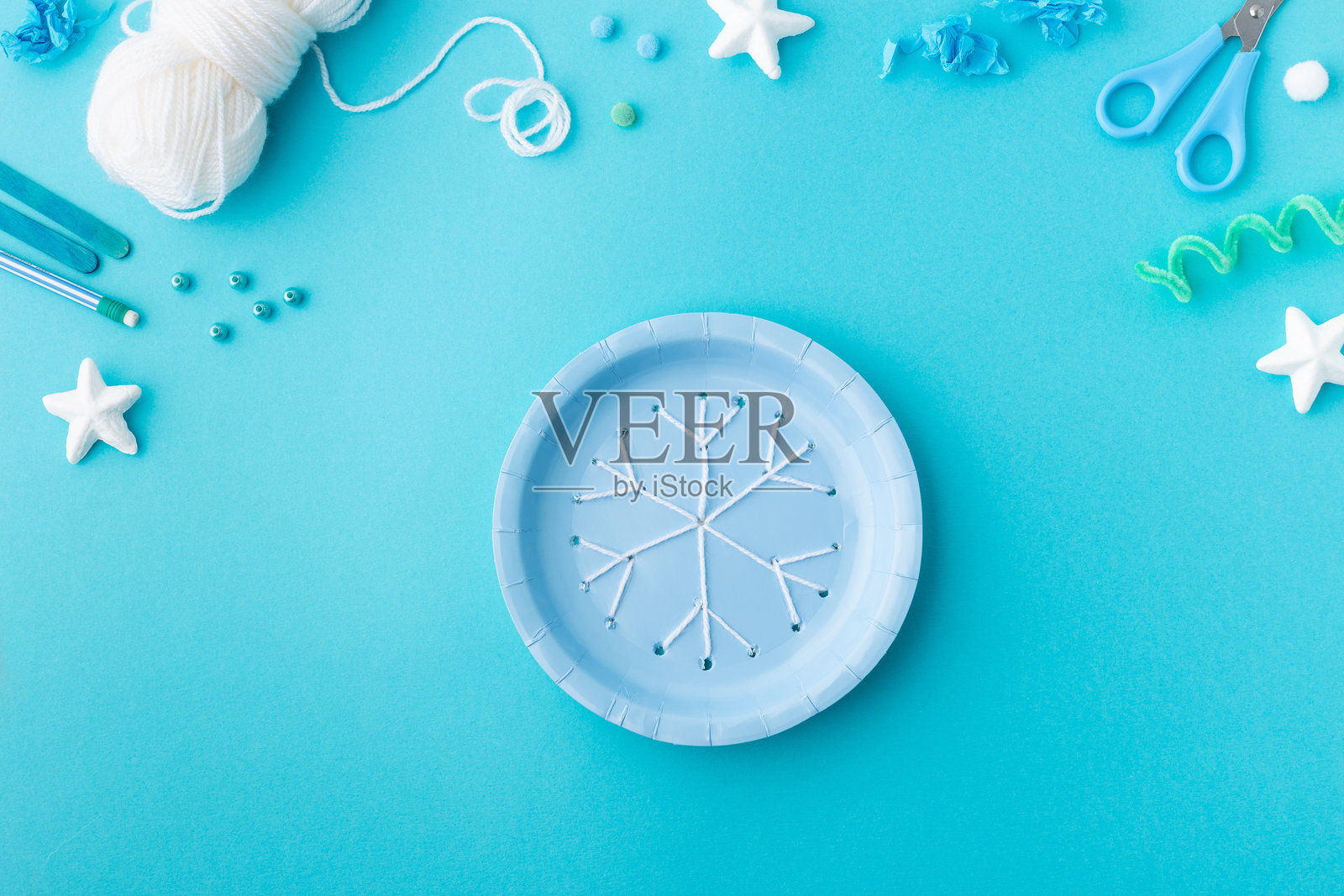 用毛线制作的雪花,放在蓝色纸盘上,适合幼儿园的圣诞创意手工。照片摄影图片