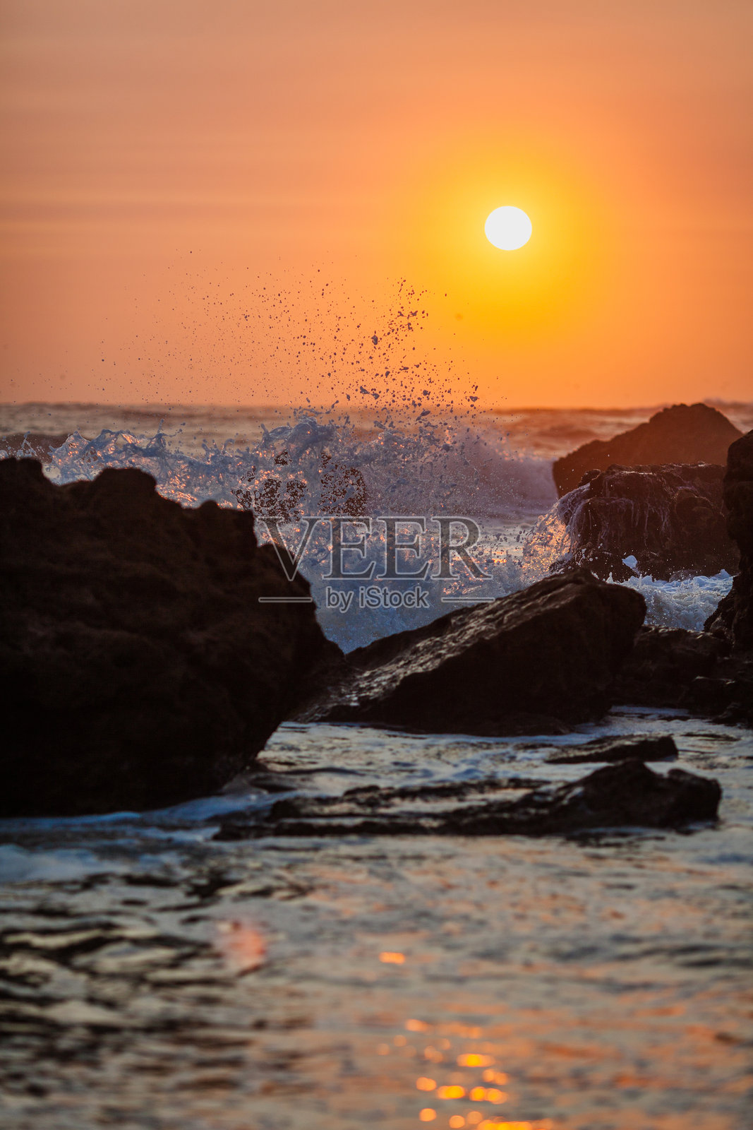 日落场景捕捉到波浪猛烈撞击岩石的强大动感,水花四溅,夕阳在地平线上缓缓落下。照片摄影图片
