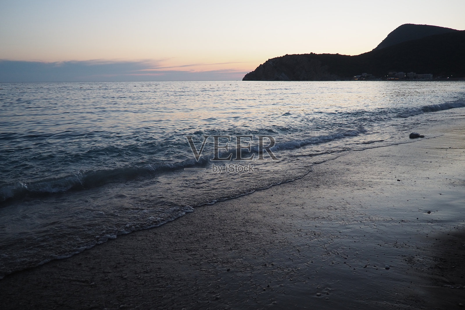 海浪轻轻拍打着海岸,壮丽的日落映照在海面上。阳光在海浪上反射,营造出海边日落时宁静的氛围。黑山的夏天。蓝色时刻。照片摄影图片