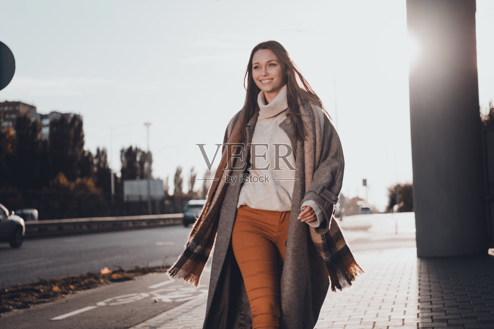 阳光明媚的户外,漂亮积极的女士露齿而笑,悠闲地走在街上。照片摄影图片