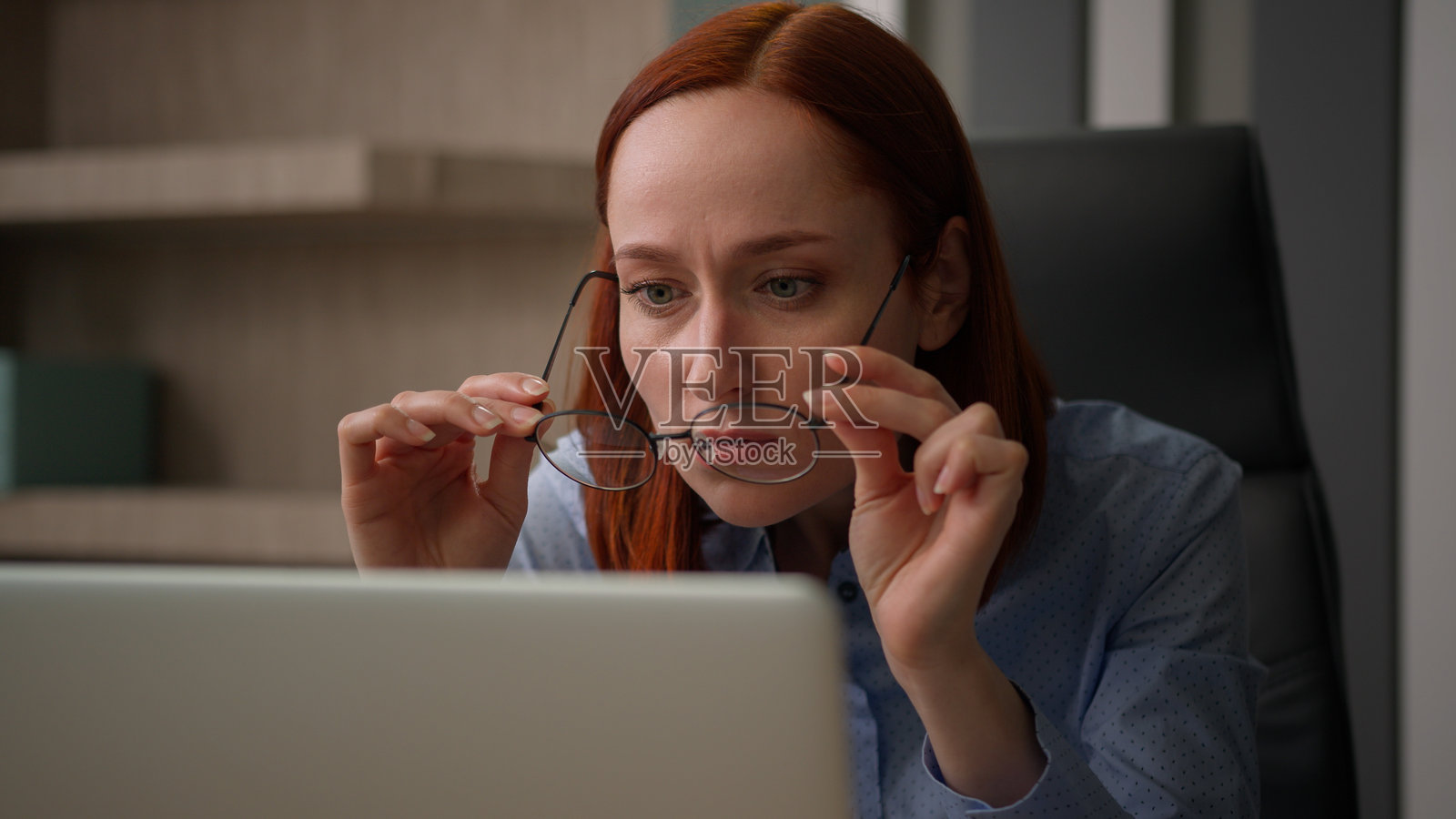 白人女商人在办公室使用电脑,坐在桌子前的女员工摘下眼镜,检查光学镜片问题,视力模糊。照片摄影图片