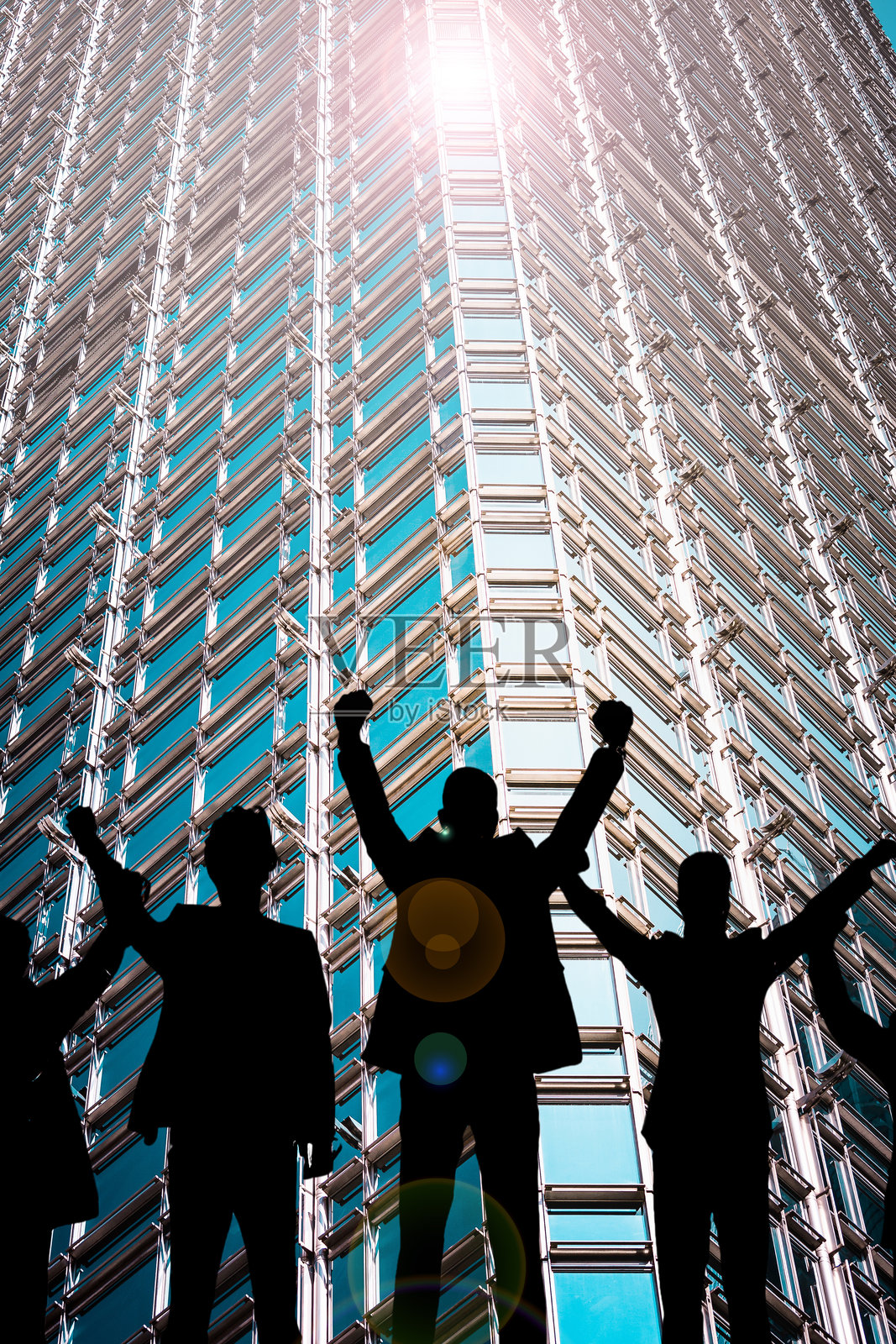 一群剪影在摩天大楼前举起双手,背景中阳光明媚。照片摄影图片