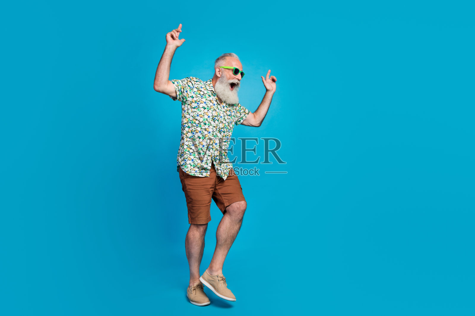 穿着酷炫夏季服装的兴奋疯狂的老爷爷,庆祝夏季服装促销,整个人全身照,背景为蓝色。照片摄影图片