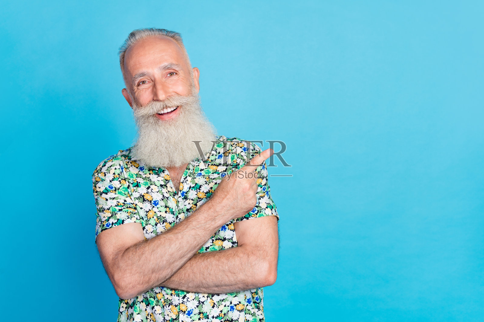 积极的老年人用手指指向蓝色背景上的空白空间。照片摄影图片