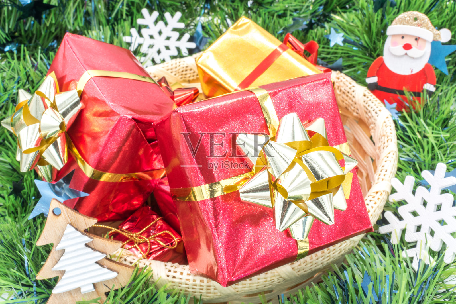 用丝带装饰的礼物的柳编篮子,周围环绕着绿色花环和一些圣诞装饰。照片摄影图片