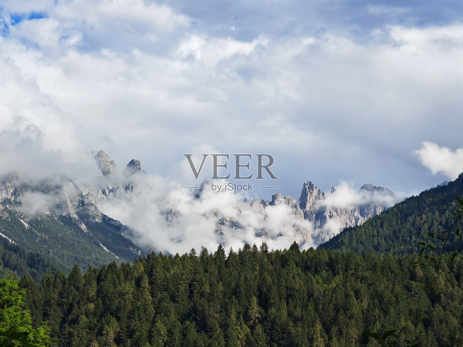 雄伟的山脉在晴朗的日子里穿越云层,矗立于郁郁葱葱的森林之上,展现了自然的美丽与宁静。照片摄影图片