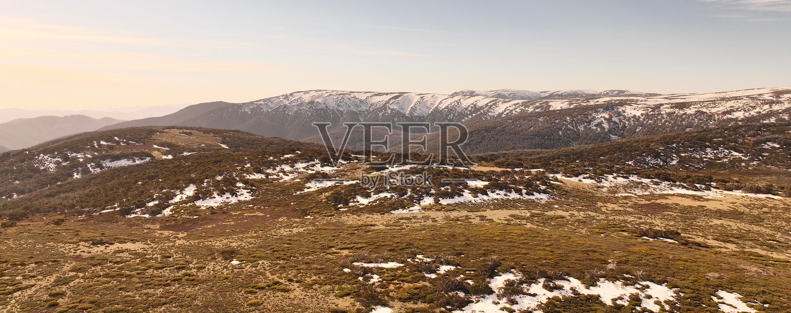 广阔起伏的景观全景,点缀着雪地和棕色植被的山脉照片摄影图片