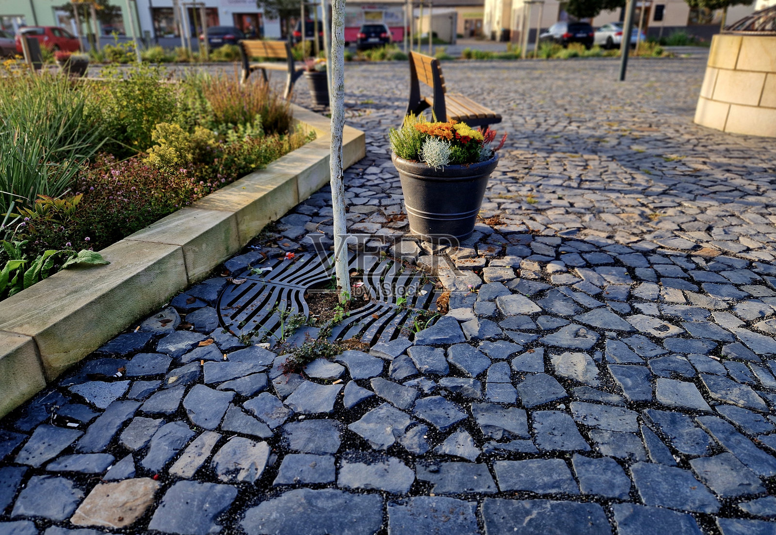 常青花坛边缘种植着一年生植物,铺设在花坛边缘的花岗岩鹅卵石镇广场上,入口处有石柱,石槽和花盆中种植着植物。照片摄影图片
