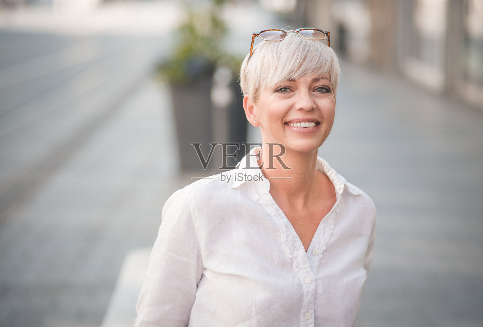 欧洲快乐的金发成年女性看向镜头。微笑的美丽中年女性穿着白色夏季衬衫。户外环境。照片摄影图片