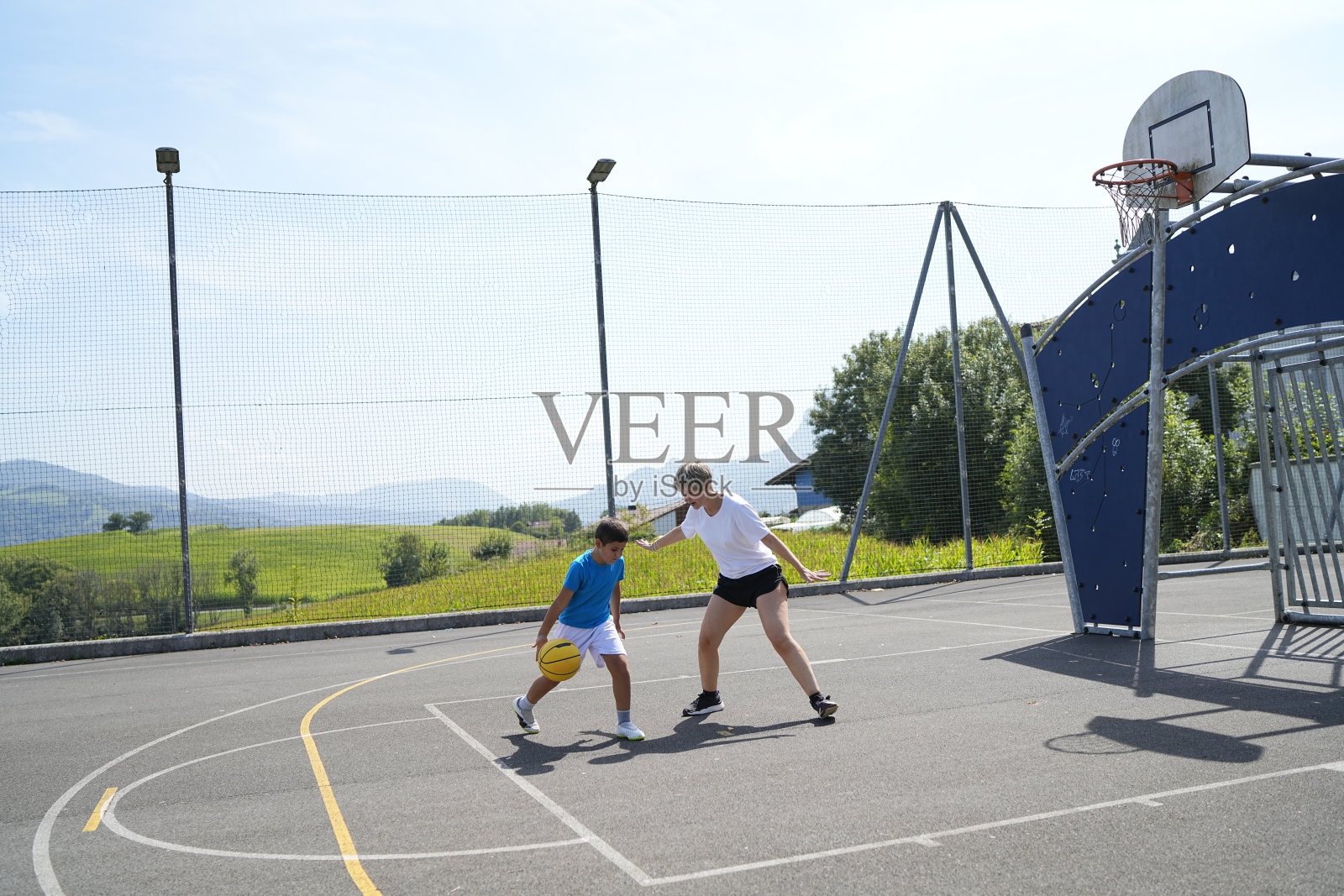 母亲在户外篮球场教儿子打篮球照片摄影图片