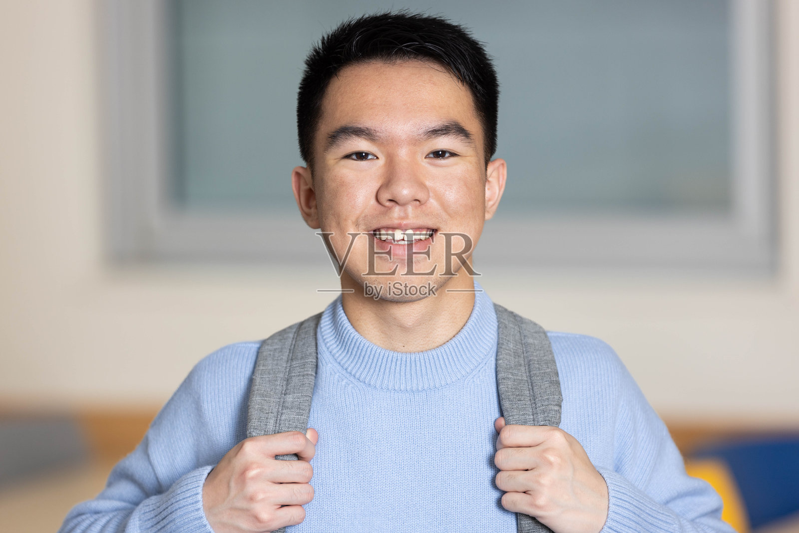 一个穿着蓝色毛衣和背包的年轻学生对着镜头微笑照片摄影图片