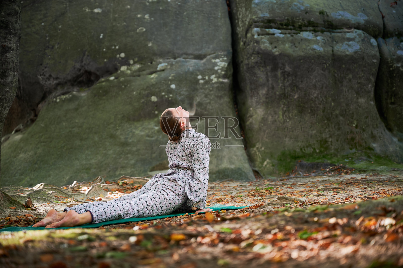 女性在森林中户外练习瑜伽。赤脚的女性在瑜伽垫上,周围是树木和岩石。照片摄影图片