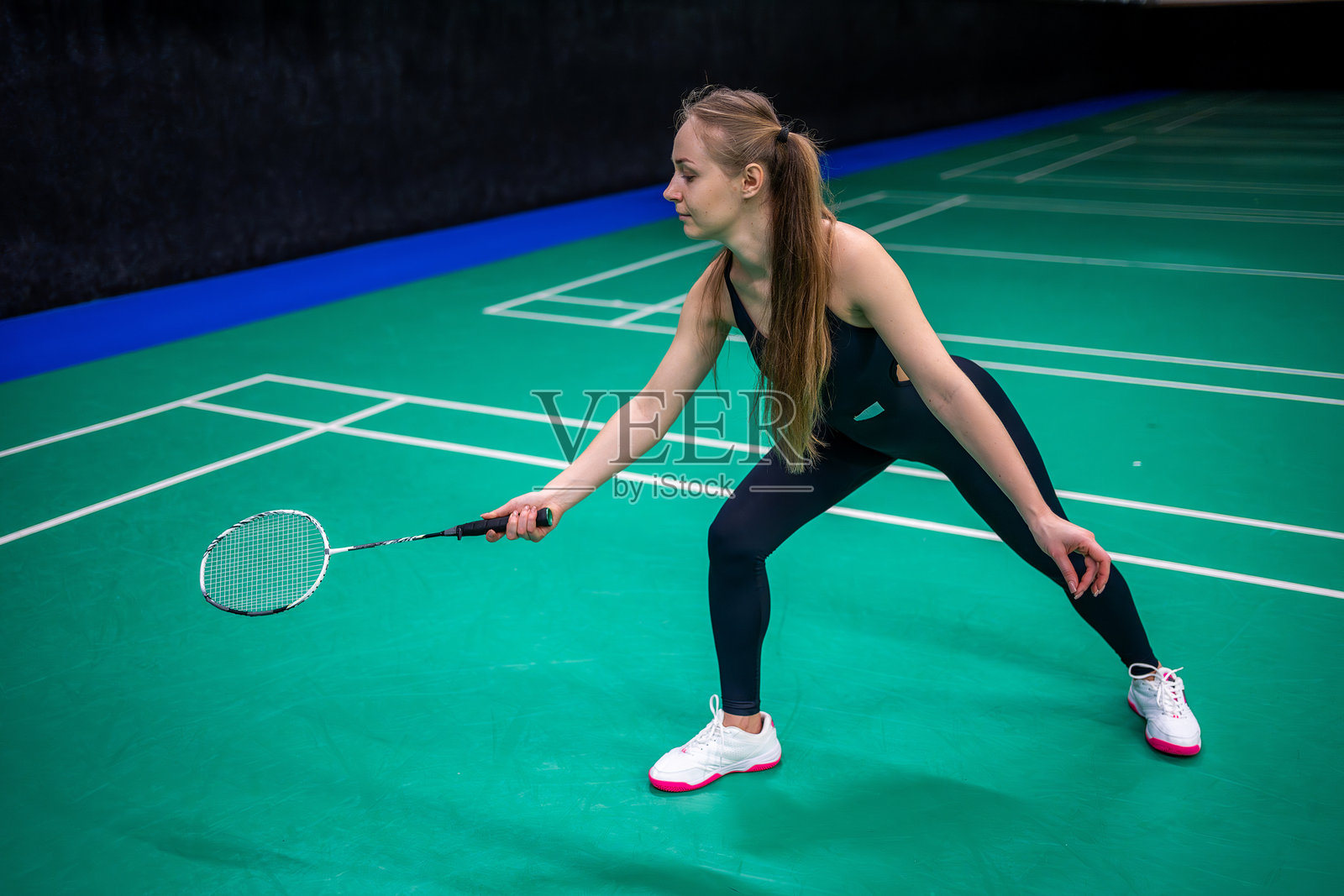 年轻女性手持羽毛球拍和羽毛球,在室内羽毛球场上摆姿势准备比赛照片摄影图片