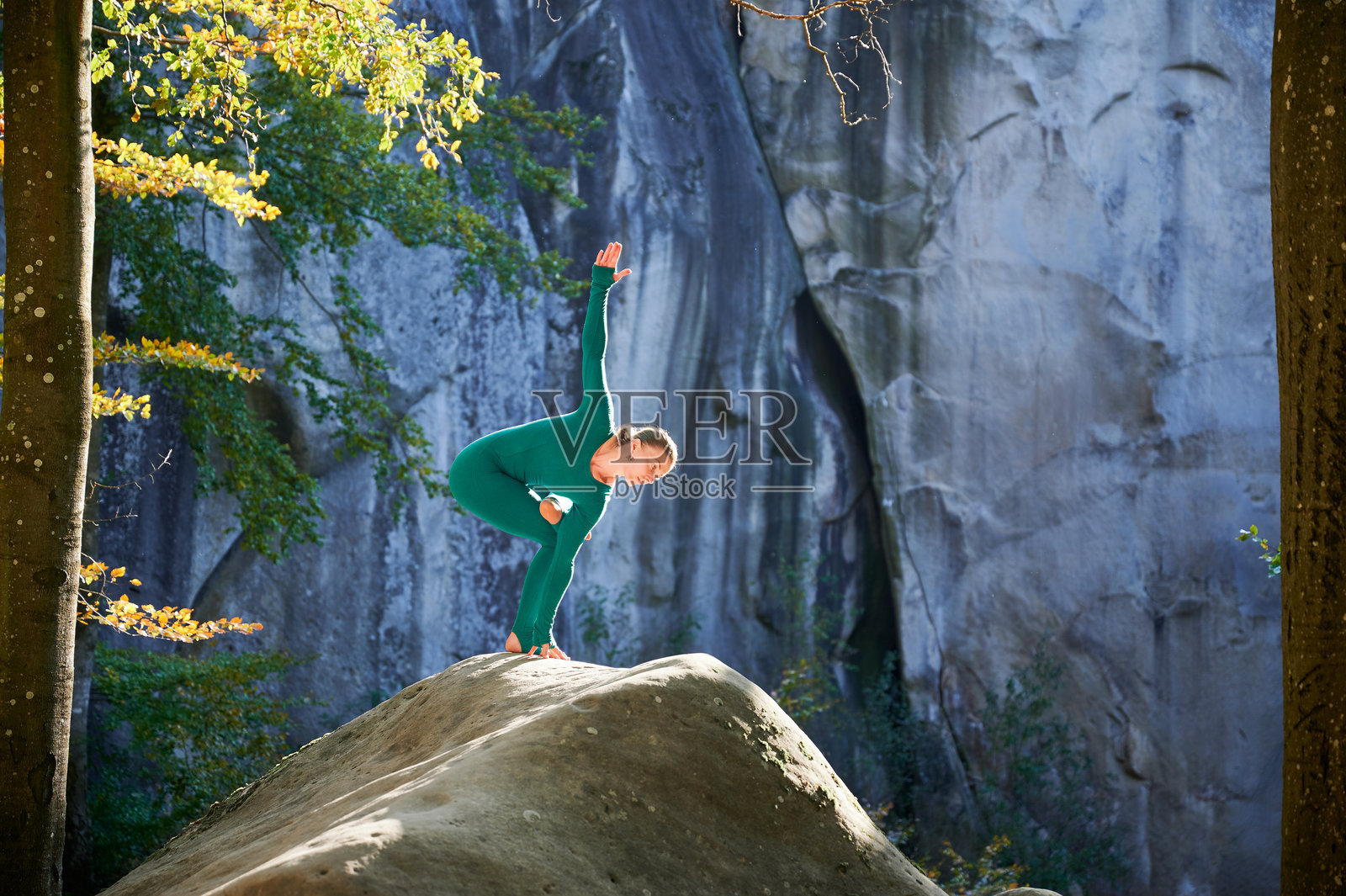 女性在森林中户外练习瑜伽。赤脚的女性站在瑜伽垫上,周围是树木和岩石。照片摄影图片
