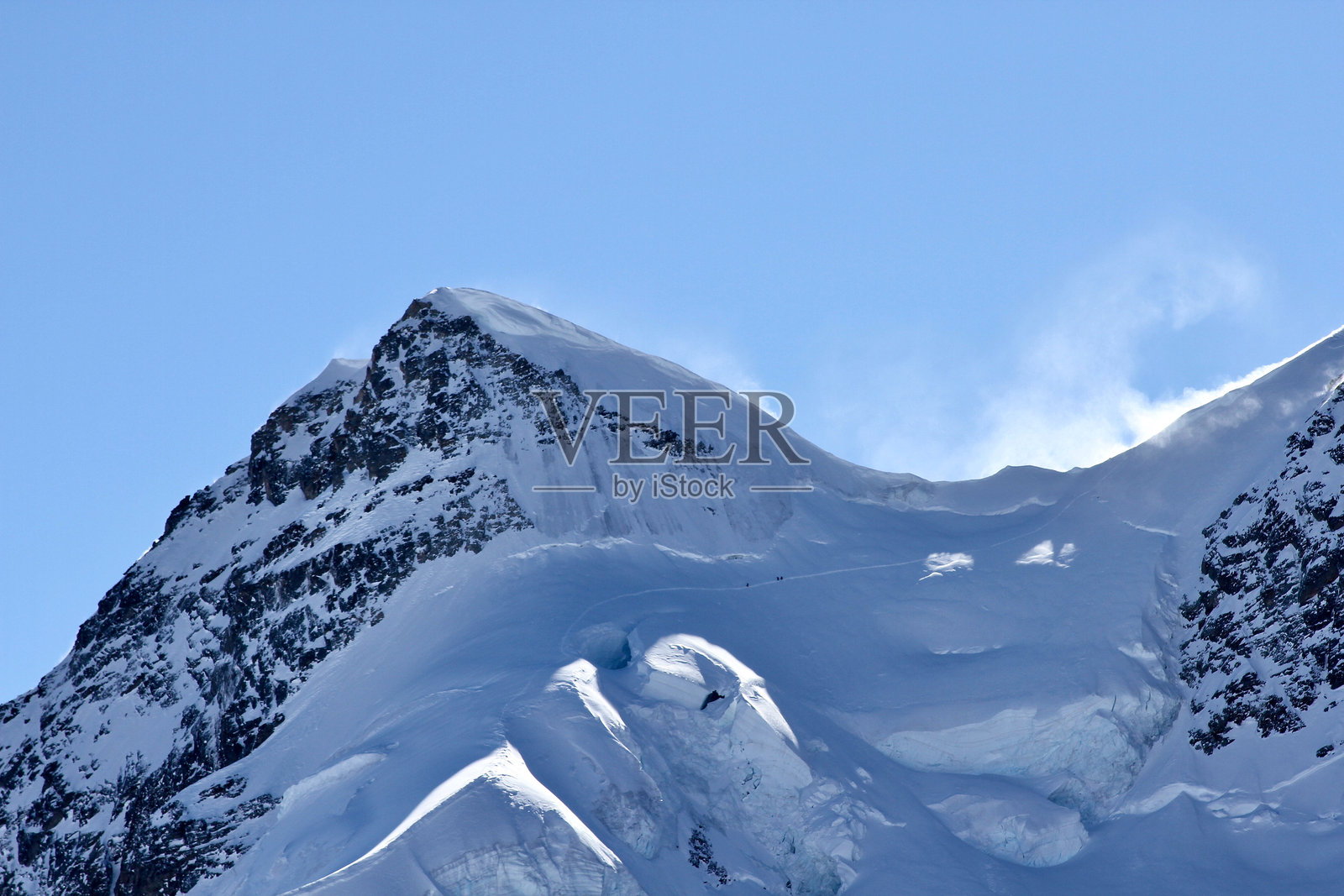 伯尔尼阿尔卑斯山脉的艾格峰,雪在鞍部随风飘扬,背景是蓝天。照片摄影图片