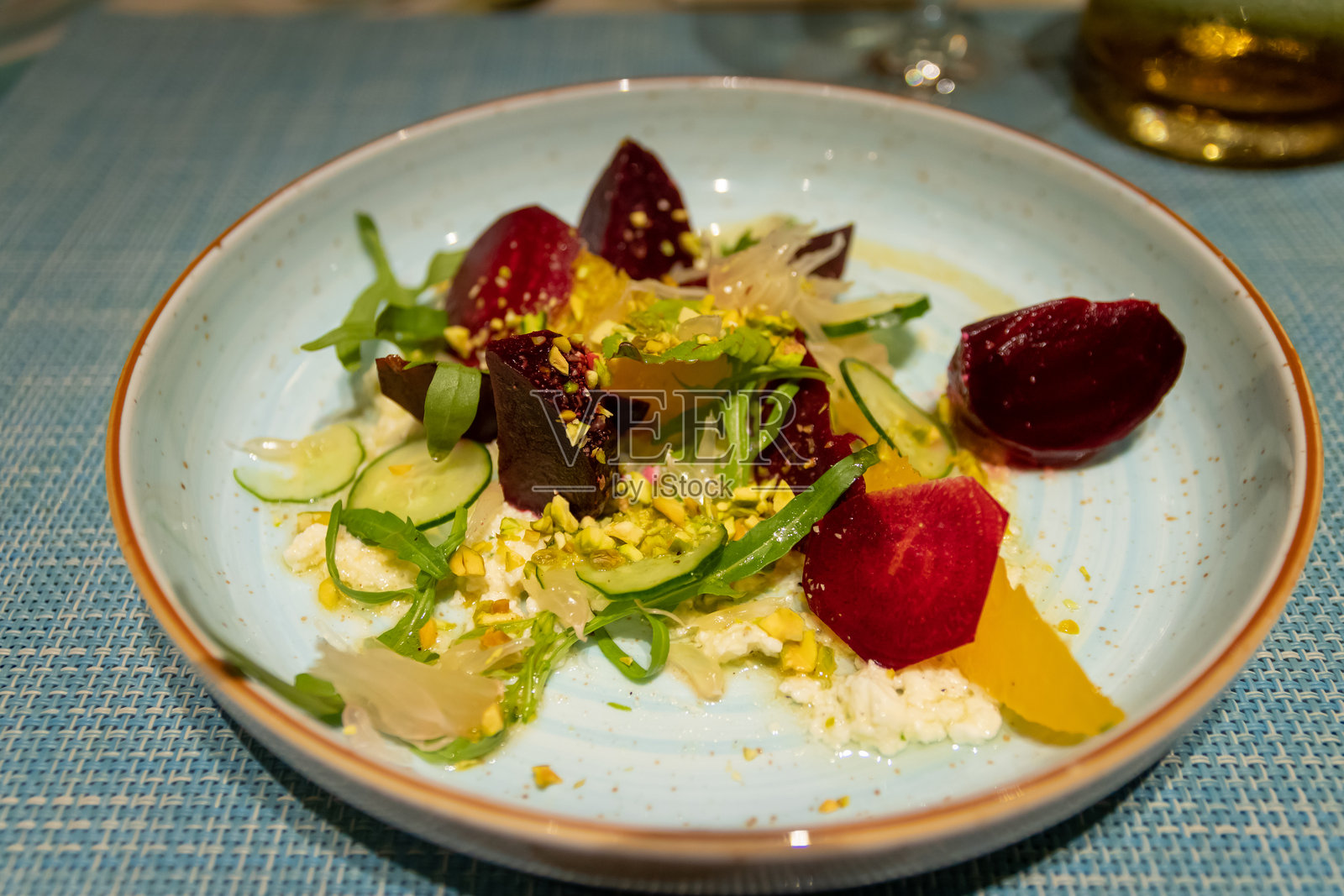 色彩鲜艳的沙拉,包含新鲜的绿叶蔬菜、甜菜和坚果,优雅地摆放在浅蓝色的盘子上。照片摄影图片