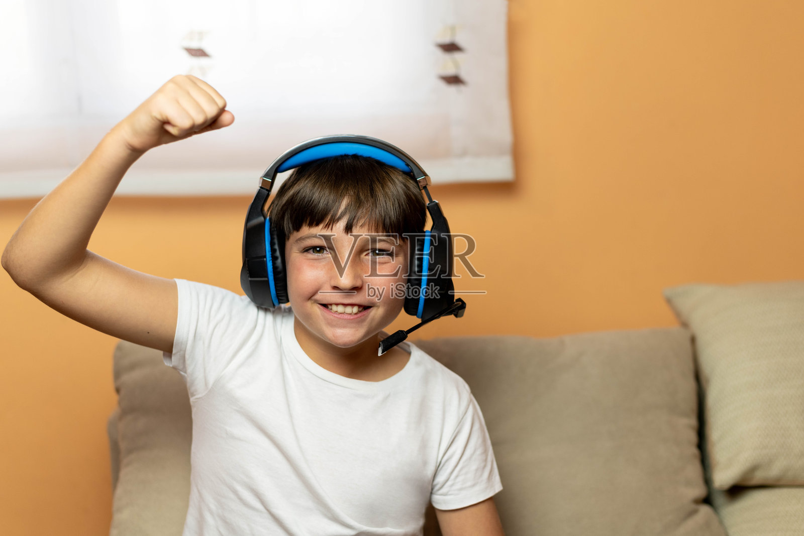 戴着耳机并举起手臂的男孩肖像。在线视频游戏胜利庆祝的概念照片摄影图片