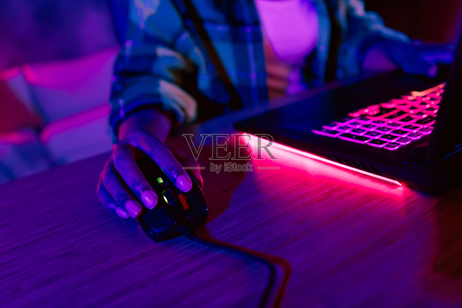 年轻女孩在昏暗的房间里玩游戏,使用有线鼠标,周围有霓虹灯光,平坦的室内环境。照片摄影图片