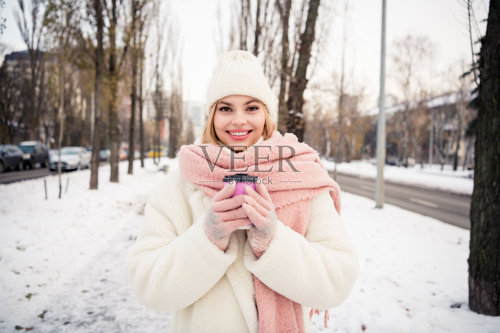 阳光明媚的漂亮女孩穿着白色夹克,在寒冷的冬日户外享受香气四溢的热饮。照片摄影图片
