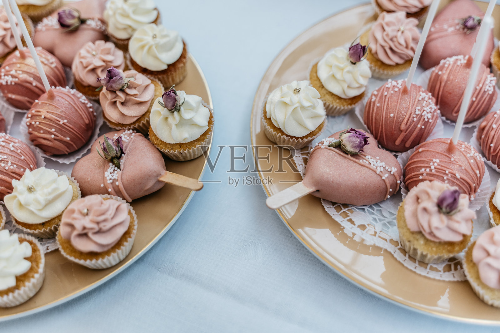 粉色蛋糕棒和杯子蛋糕,上面装饰有干玫瑰花蕾和珍珠糖霜照片摄影图片