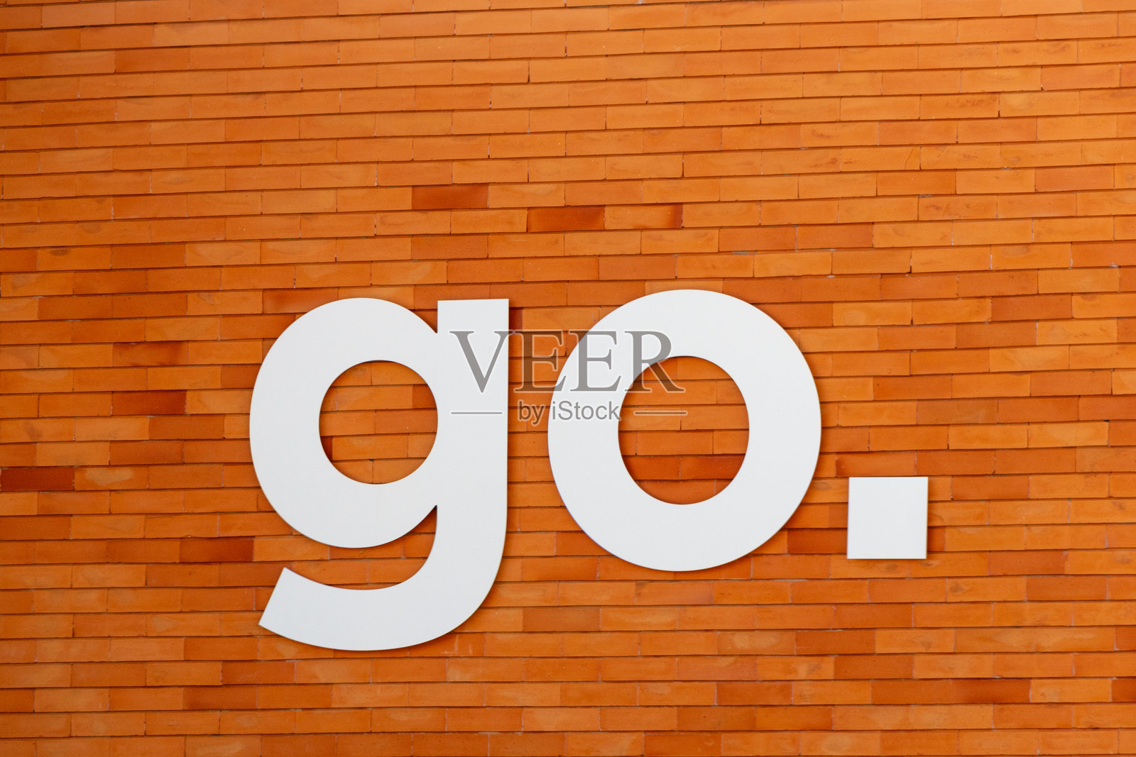 固定在橙色砖墙上的大型白色“走”标志照片摄影图片