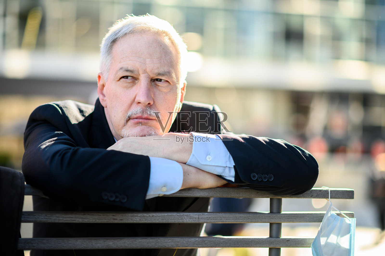 沉思的商人坐在长椅上,口罩挂在耳边:疫情期间的思考照片摄影图片