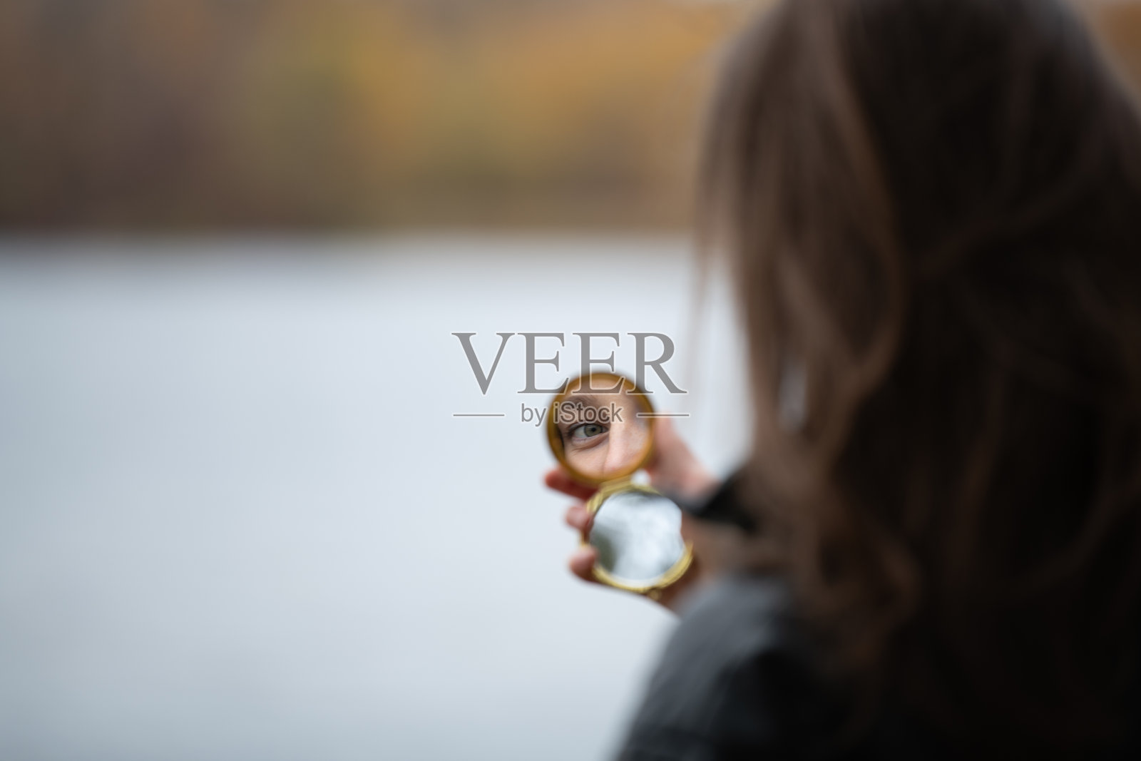 一位女性在宁静的湖边用口袋镜子检查自己的倒影,正值初秋时节。照片摄影图片