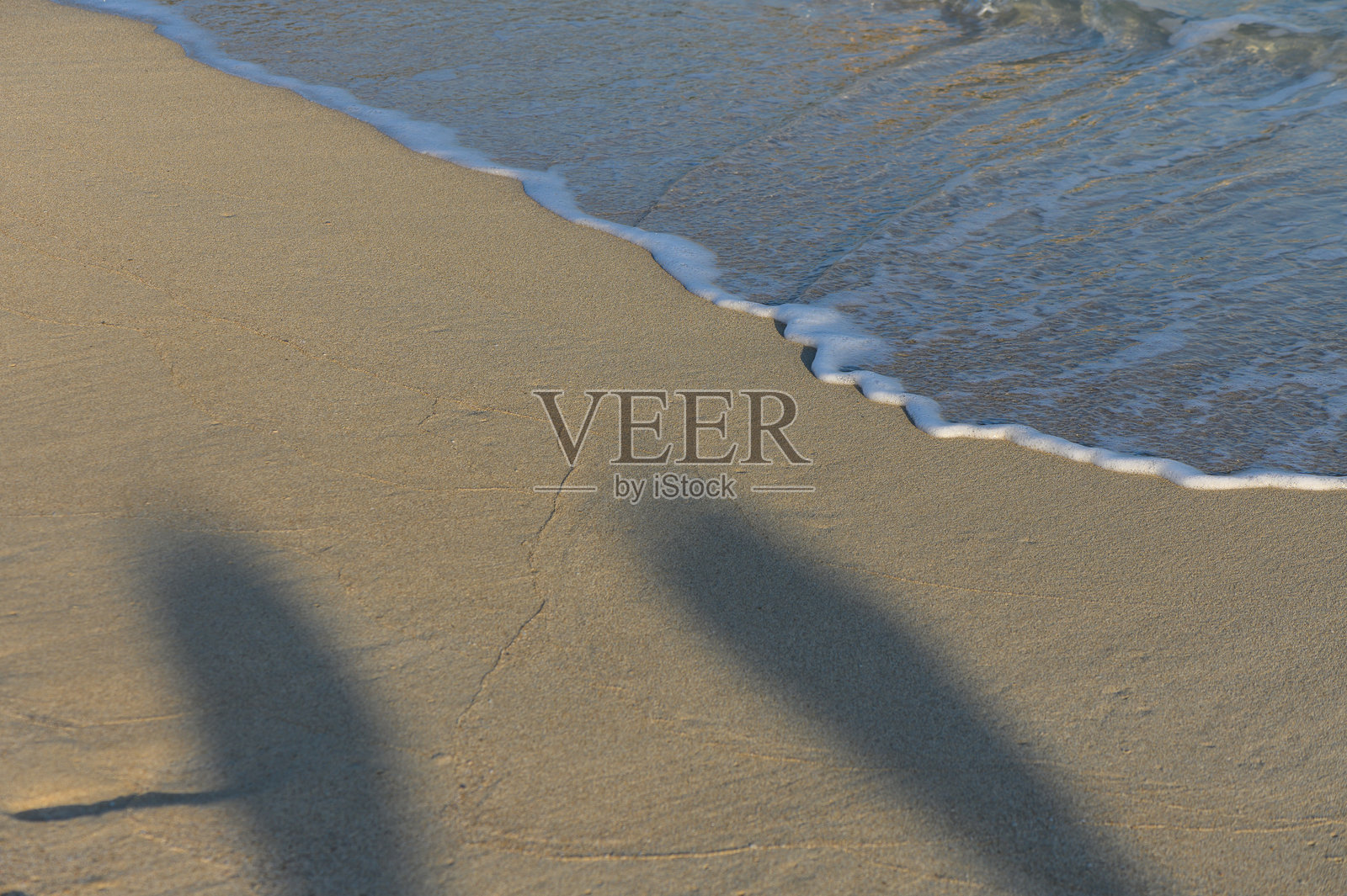 两个人影在海岸边嬉戏,柔和的海浪轻轻拍打着沙滩,投下了阴影。照片摄影图片