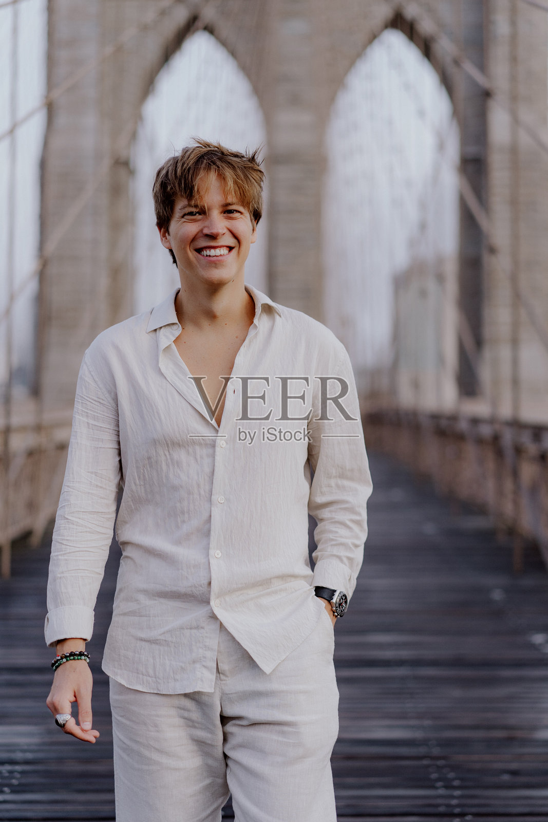 一位年轻男子在标志性的布鲁克林大桥上愉快地微笑,穿着休闲。照片摄影图片