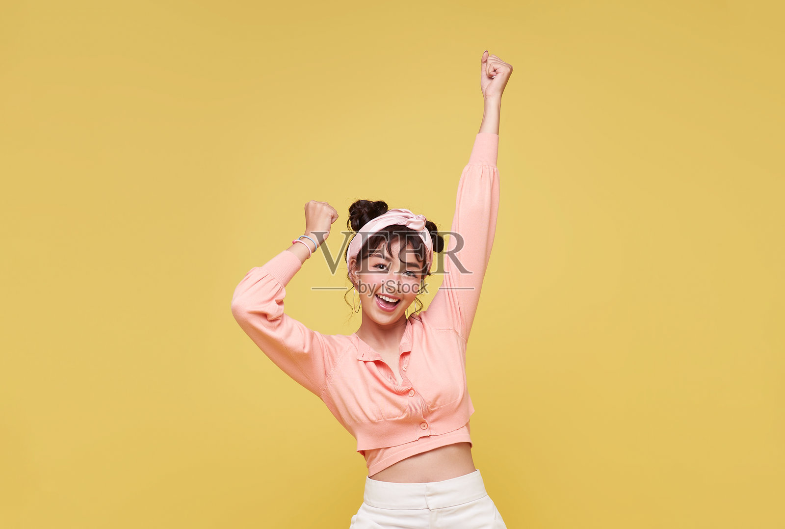 迷人的亚洲少女站立,双手高举庆祝,背景为黄色。照片摄影图片