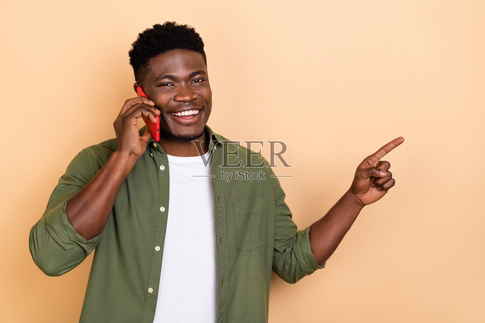 一位印象深刻的千禧一代棕发男士穿着休闲服装,手持电话,背景为米色。照片摄影图片