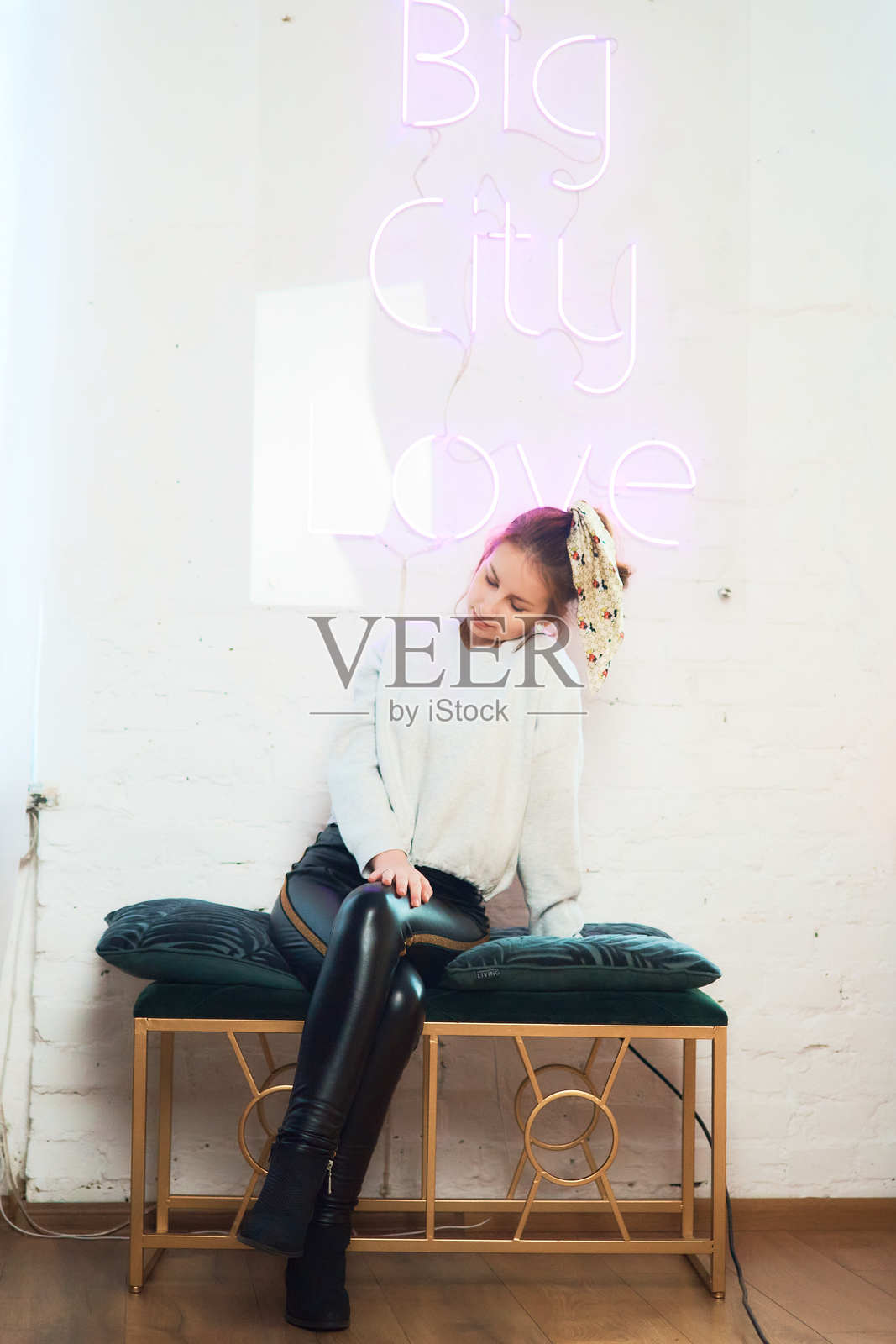 一位青少年女孩在白色墙壁旁,旁边有粉色霓虹灯标志,摄影棚拍摄。照片摄影图片