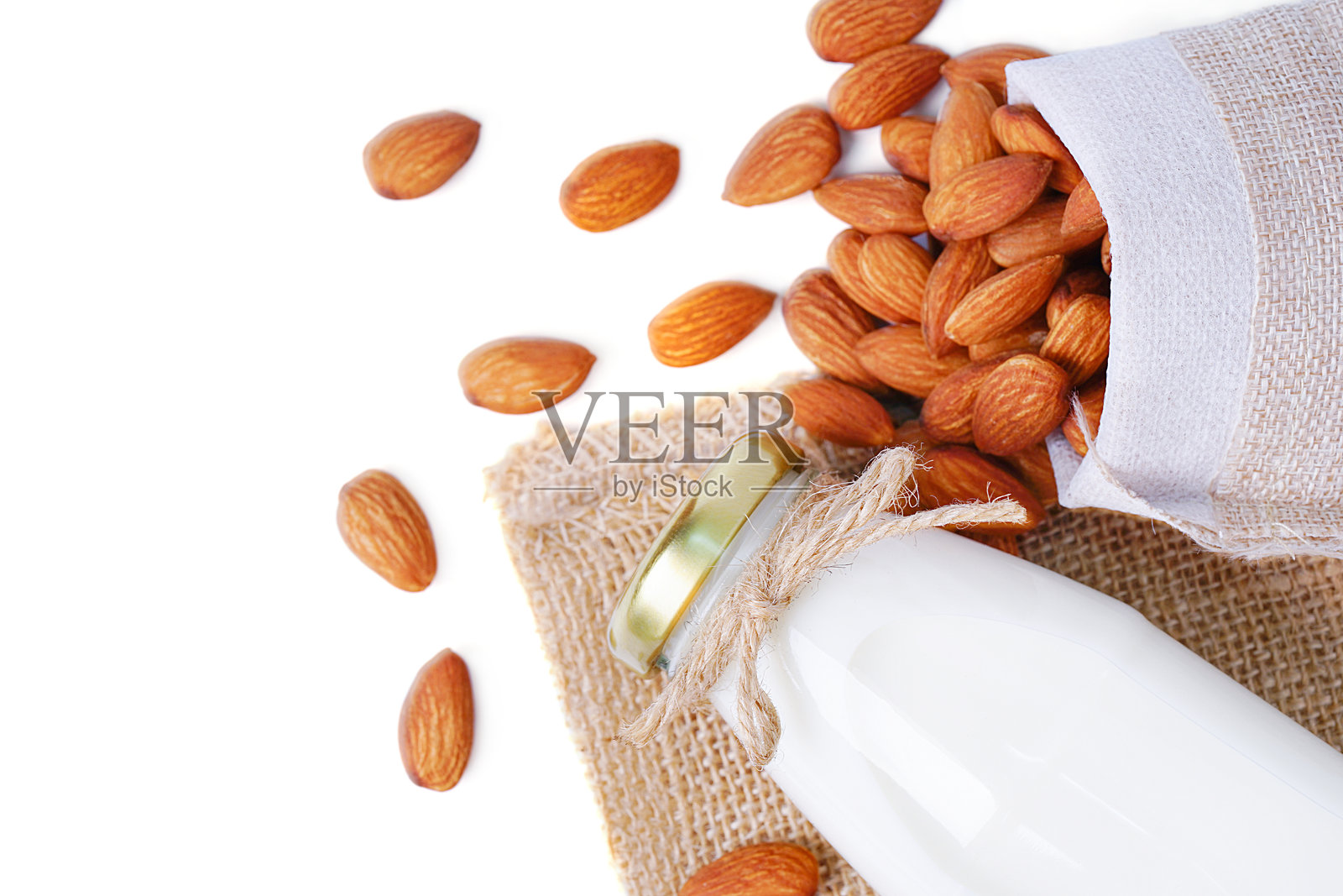 顶部视角的玻璃牛奶瓶,装有杏仁,放在孤立的麻布袋中照片摄影图片